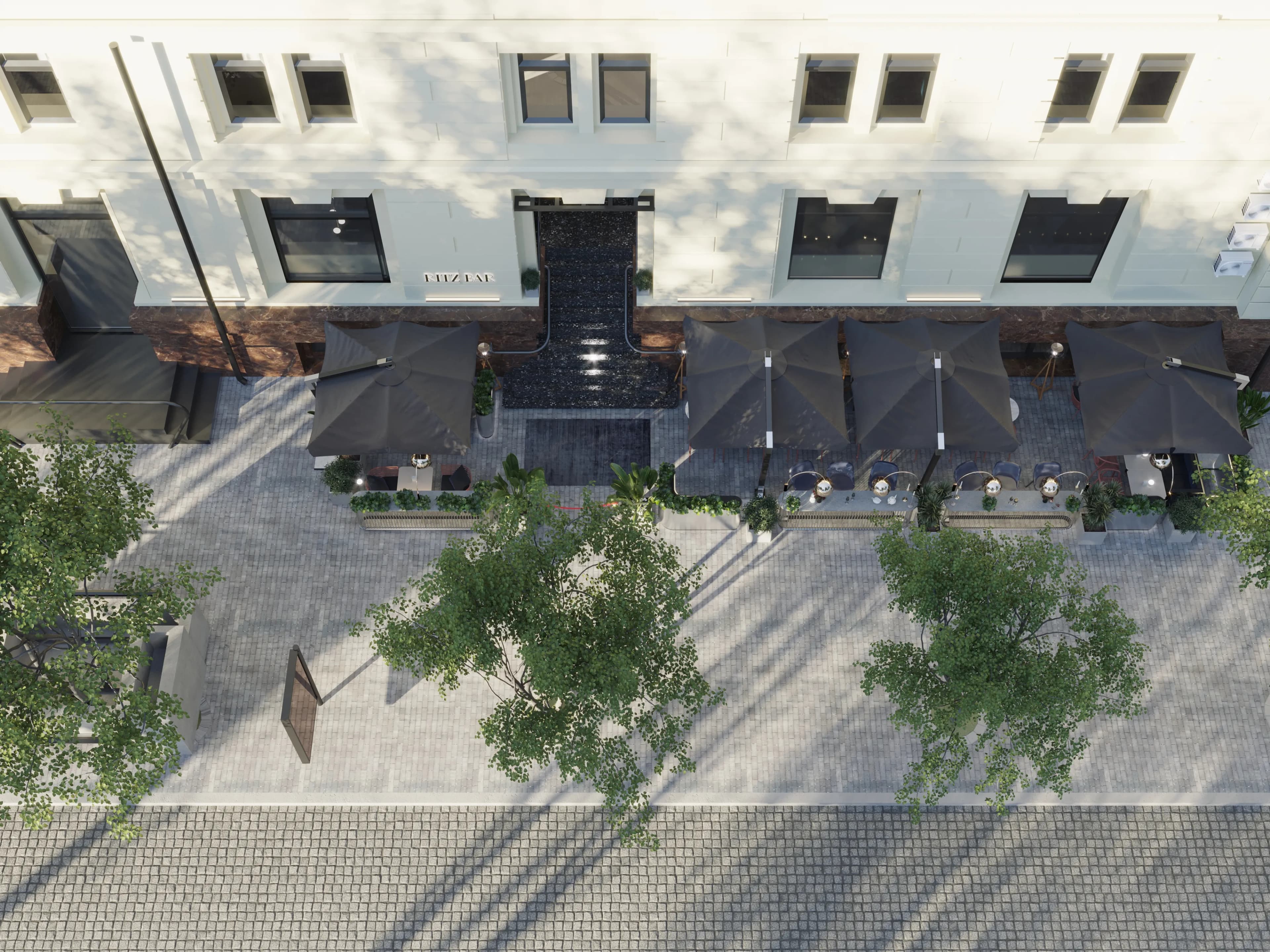 aerial view of a white building facade with dark umbrellas of a summer terrace, trees and a cobbled pavement